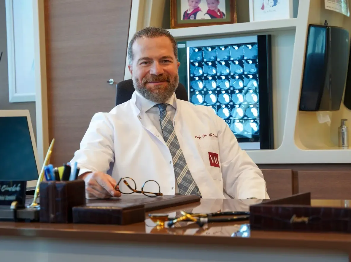 Prof. Dr. Ali Civelek muayenehanesinde, beyaz önlükle masasında