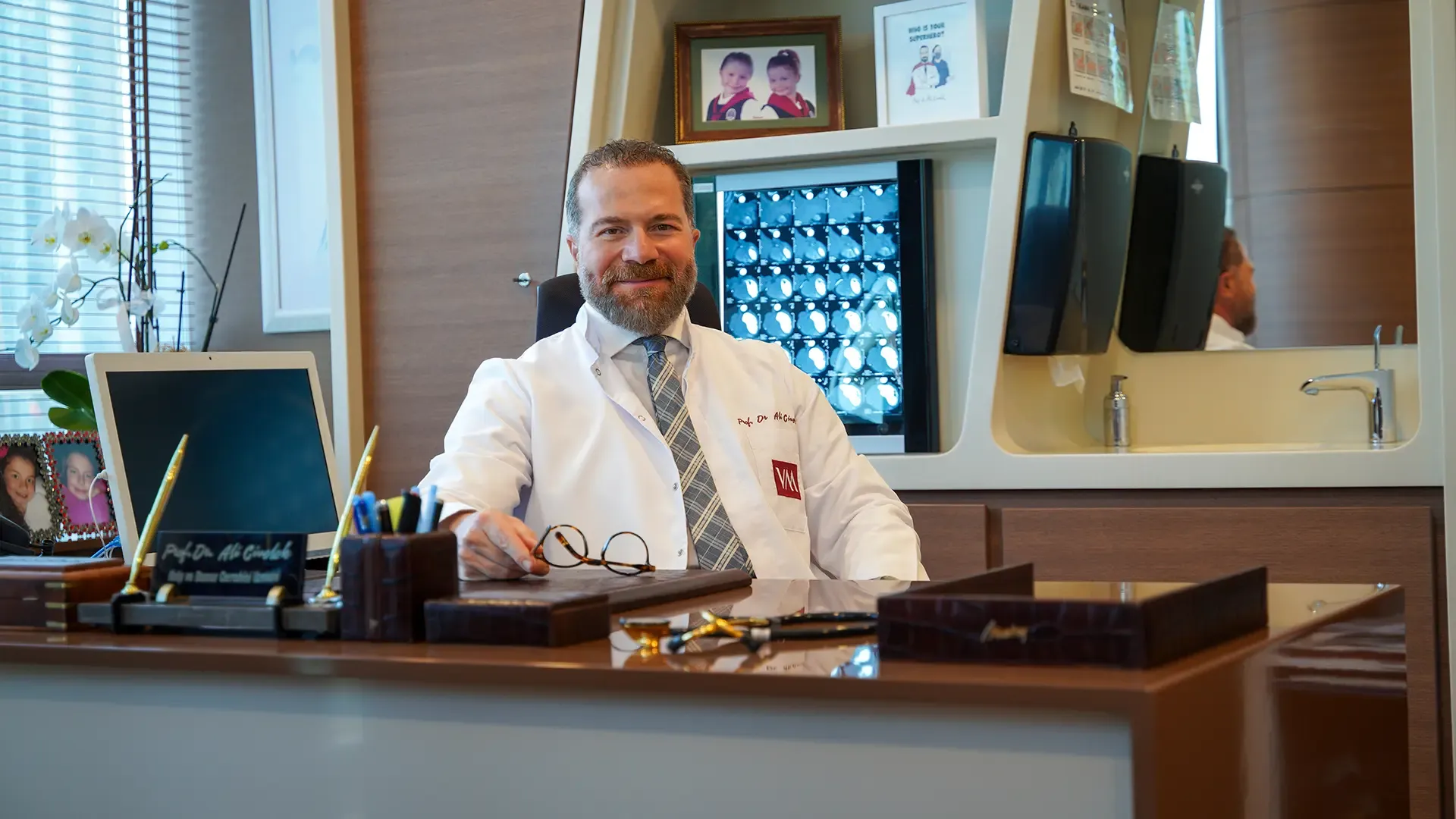 Prof. Dr. Ali Civelek muayenehanesinde, beyaz önlükle masasında